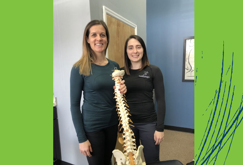 Two female students holding skeleton anatomical model.