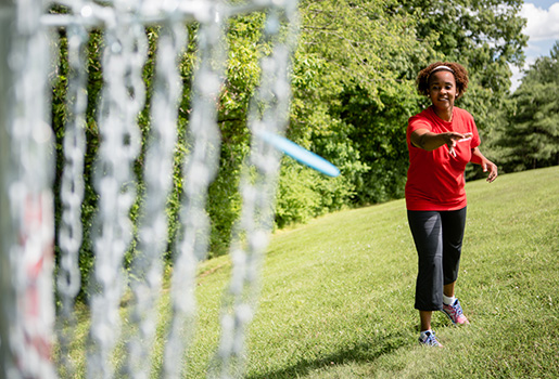 Female student playing disc golf on campus.