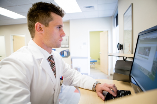 A male health center clinician consults with a patient via telehealth on a desktop computer