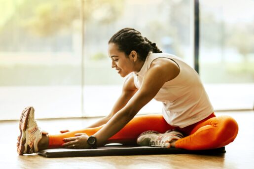 Women in white tank top and orange leggings stretches on the ground