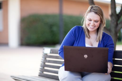 A woman sits on a bench with a laptop